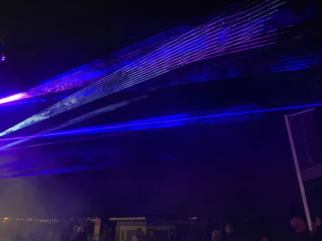 Blue laser beams fanning over a seafront crowd at night